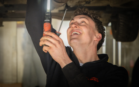 Lachende monteur aan het werk onder een auto